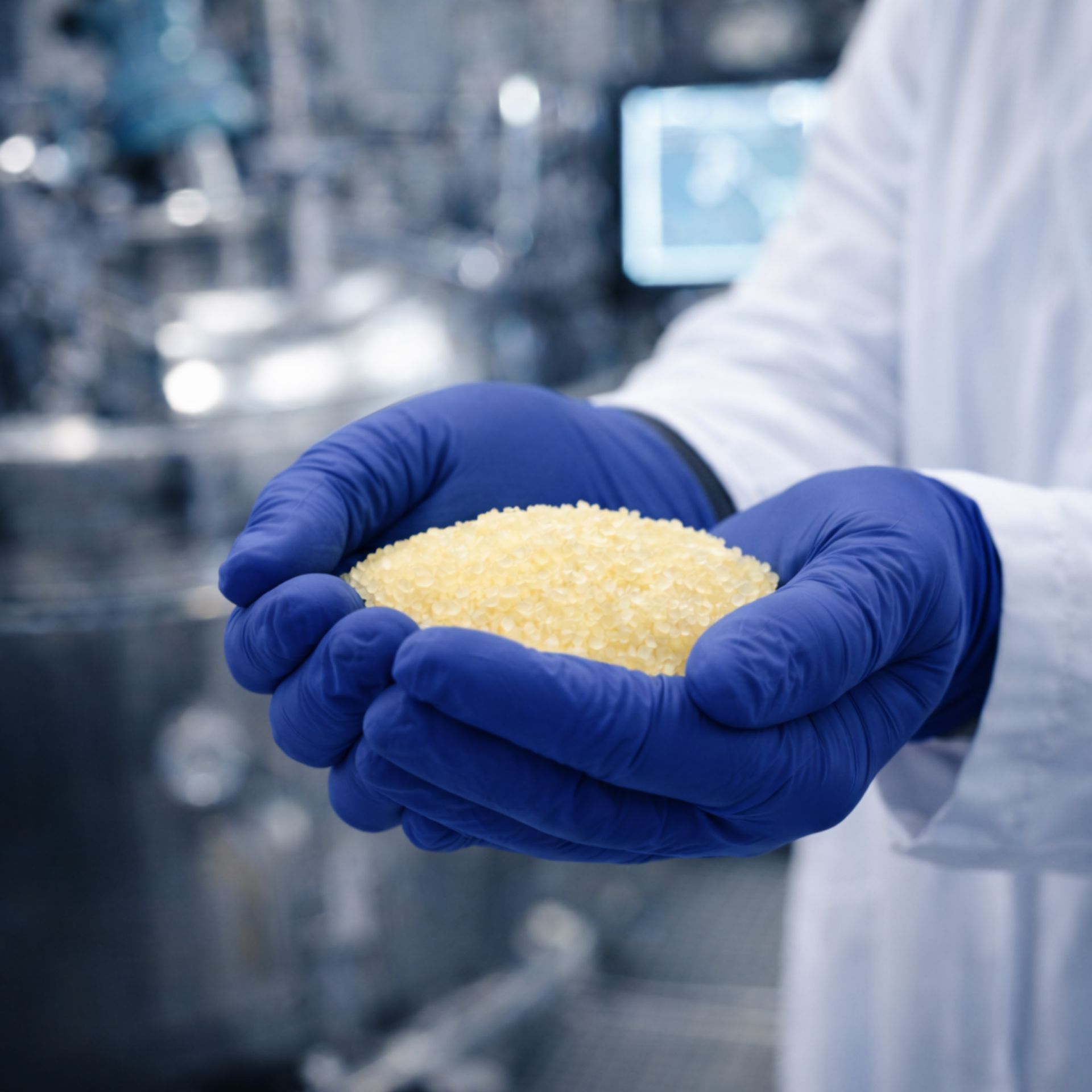 Gloved hands holding yellow gelatin granules in an industrial manufacturing facility.