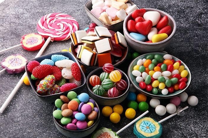 Colorful assorted candies and gummies in bowls on a dark surface.